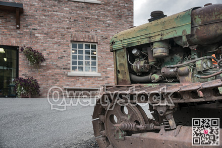 Old rasty tracked tractor in front of brick building