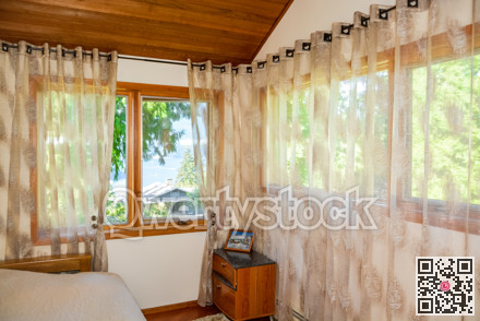 Wide windows and curtains in small bedroom with ocean bay view.