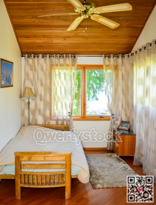 Small lightful bedroom with curtains on windows and rug on the floor.