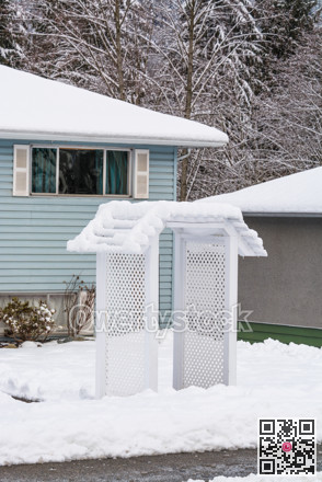 Residential house front yard in snow with entrance arch over pathway