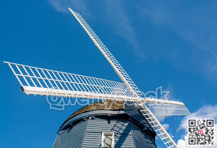 Top of vintage wind mill decorated with lights on blue sky background.