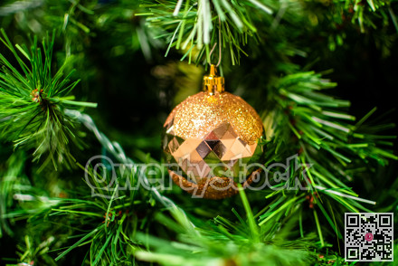 Golden bauble among chistmas tree brenches. Closeup look of the ball.