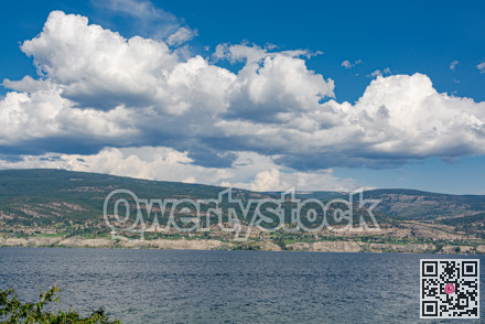 Overview of Okanagan lake with mountains and clouds on blue sky background.
