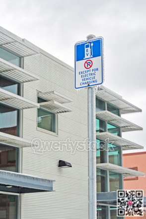 Road sign of EV charging station covered with icicles on overcast sky background