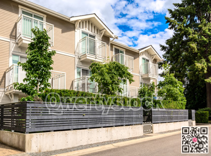 Residential condo building with fenced front yard on bright sunny day