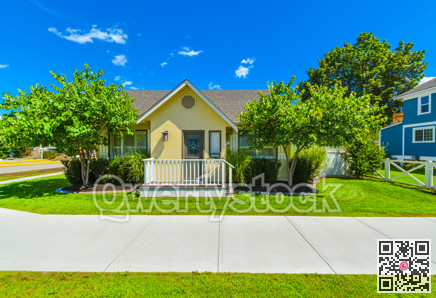 Small yellow family house on sunny day with green lawn and concrete pathway