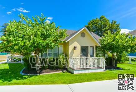 Small yellow family house on sunny day with green lawn and concrete pathway