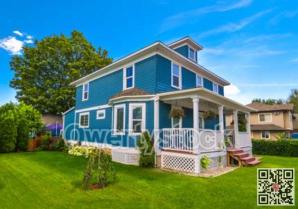 Historic family house with green lawn in front and blue sky background.
